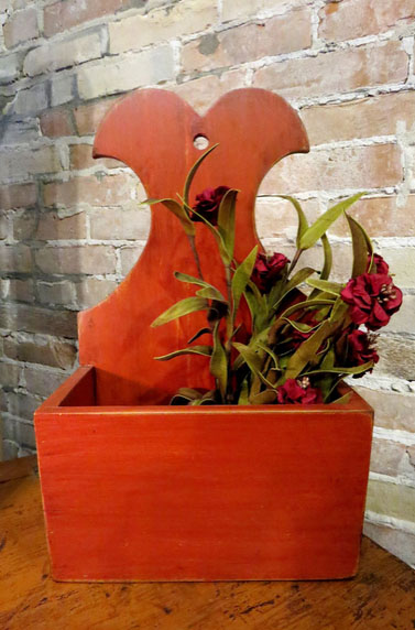 Online, John & Kaye's "Colonial Candlebox" is described and sold as, "Distressed redish/orange with dark brown stain. Box measures 14"h x 8.5" w x 4.75" d. Sorry does not include flower pick."